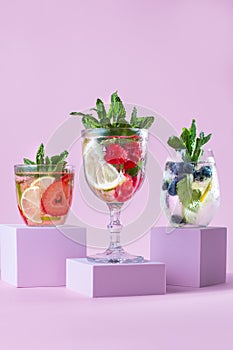 Summer refreshing fruit and berry infused detox water on podiums in pink color, creative summer beverages background