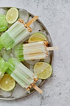 Summer refreshing homemade lime popsicles with chipped ice over stone background