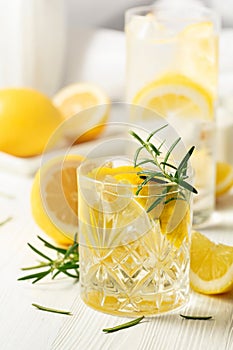 Summer refreshing lemonade drink or alcoholic cocktail with ice, rosemary and lemon slices on the white table