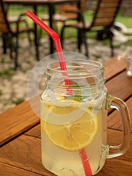 Summer refreshing mojito lemonade in glass jar mug with slice of lemon, ice, red straw and mint