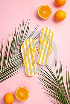 Summer rest concept. Top view vertical photo of yellow striped flip-flops juicy oranges and palm leaves on isolated pastel pink