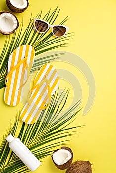 Summer rest concept. Top view vertical photo of yellow striped slippers sunglasses sunscreen bottle cracked coconuts and palm