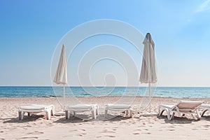 Summer rest on sea beach background. Deckchair or sunbeds with umbrellas on white sand of resort beach on sunny clear day