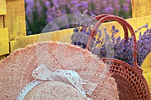 Summer rest. Woman\'s straw hat and basket with bouquet of lavender on wooden bench on blooming field of purple flowers