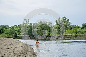 In the summer on the river the boy runs along the shore.