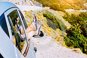 Summer road trip car vacation concept. Woman legs out the window in car on the winding road of greek island