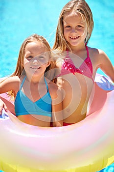 Summer rocks. Two little girls using an inflatable tube while getting ready to swim.