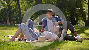 Summer romance. Happy couple in love enjoying picnic in public park, man feeding woman with ripe strawberries