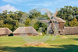 Summer rural old landscape with a wooden windmill and the master`s huts under a thatched roof