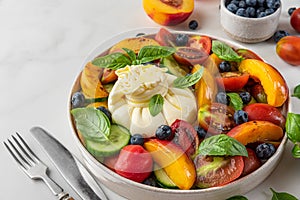 Summer salad with burrata cheese, grilled peaches, tomatoes, blueberries, cucumber, olive oil and basil. Top view