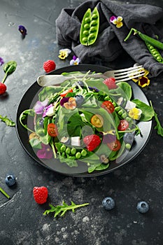 Summer salad with edible flowers, spinach, blueberries, raspberry, sweet peas, cherry tomatos and feta cheese