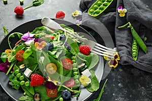 Summer salad with edible flowers, spinach, blueberries, raspberry, sweet peas, cherry tomatos and feta cheese