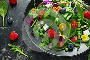 Summer salad with edible flowers, spinach, blueberries, raspberry, sweet peas, cherry tomatos and feta cheese