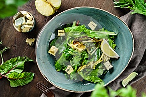 Summer salad with leaves of lettuce, spinach, apple, blue cheese and lemon juice in plate on wooden background. Healthy vegan food