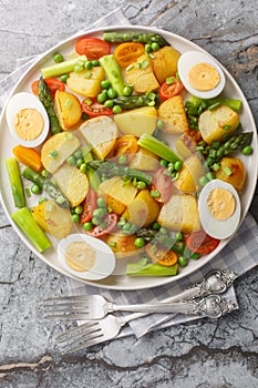 Summer salad with potatoes, green peas, asparagus, boiled egg and tomato closeup on the plate. Vertical top view