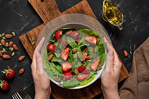 Summer salad with strawberries in female hands. Salad with fresh strawberries, arugula, spinach, seeds and nuts. Vegan and