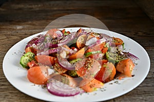 Summer salad of tomatoes, cucumbers, spices and herbs in a white plate on a wooden table.