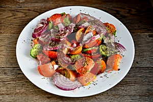 Summer salad of tomatoes, cucumbers, spices and herbs in a white plate on a wooden table.