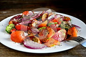 Summer salad of tomatoes, cucumbers, spices and herbs in a white plate on a wooden table.