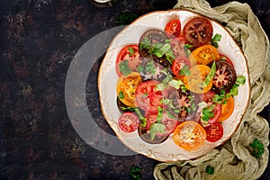 Summer salad of tomatoes of different colors with green herbs and pepper.