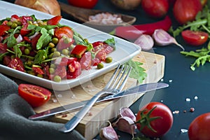 summer salad, tomatoes, green peas, arugula, onion, olive oil, garlic, hot pepper fork knife bamboo cutting board pastel green