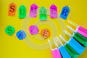 Summer sale written on colorful sale tags on bright yellow background with shopping paper bags/summer shopping concept