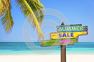 Summer sale written on pastel colored wooden direction signs, beach and palm tree background