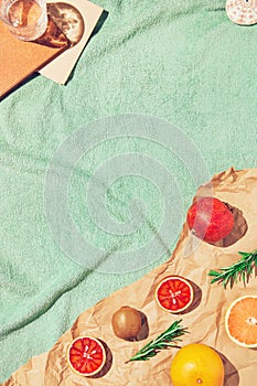 Summer scene with fruits,rosemary, glass of water and books on pastel green beach towel. Drinks and refreshment concept. Sunlit