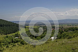 Summer scene with mountain glade, forest and residential district of bulgarian Zhelyava village, Sofia region, Balkan mountain