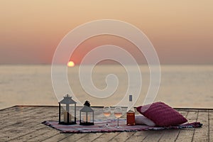 Summer sea sunset. Romantic picnic on the beach. Bottle of wine, glasses, candles, plaid and pillows.