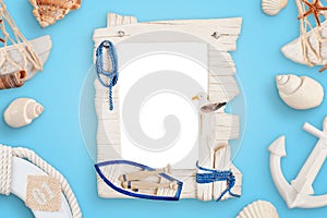 Summer sea travel photo frame on blue desk surrounded with shells, boat anchor, lifebelt