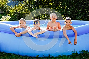 Summer season concept background. Four happy friends in an inflatable pool in the garden, refreshing themselves in hot weather