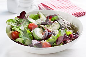 Summer season salad with salad leaves, tomatoes, cucumbers, Italian herbs and cheese in a bowl on a table