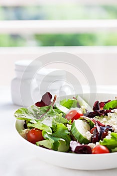 Summer season salad with salad leaves, tomatoes, cucumbers, Italian herbs and cheese in a bowl on a table