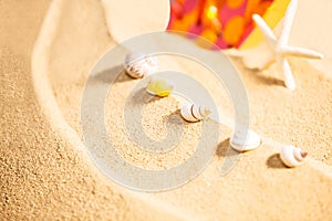 Summer Season, selective focus on seashells with starfish and spotty sandals or dotty flip-flop on sandy beach background