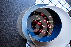 Summer season. Sweet dark cherries in a ceramic bowls on a dark background and kitchen towel with a blue lines