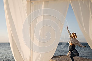 Summer shot, through white canopy on seashore of caucasian young pretty girl standing on pier.