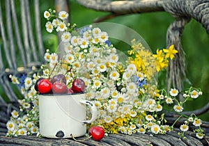 Summer simple still life. Sweet cherry in an iron mug and a simple bouquet of summer field flowers. Vintage style. summer on the f