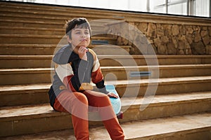 Summer skateboarding, active lifestyle. Sports recreation. Handsome schoolboy skateboarder sitting on steps outdoors