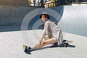 Summer. Skater Girl Sitting On Skateboard At Skatepark Portrait. Female Teenager In Casual Outfit Looking At Camera.