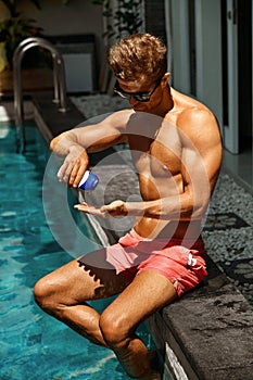 Summer Skin Care. Man Applying Tanning Sun Cream Near Pool