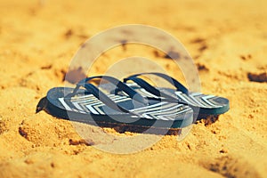 Summer slippers. Navy blue flip flop on yellow sand beach background. Copy space, top view. Holiday and travel concept