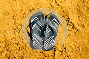 Summer slippers. Navy blue flip flop on yellow sand beach background. Copy space, top view. Holiday and travel concept