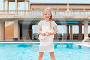 Summer. A small Caucasian girl laughing merrily. Outdoor. In the background is a complex with a swimming pool. The