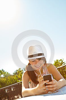 Summer, smoothies and cellphones. A happy teenage girl texting on a smartphone while enjoying a smoothie at an outdoor