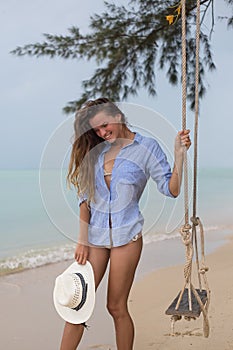 Summer solar portrait of fashion of a way of life of the young stylish woman,sitting on a swing on the beach,carrying lovely fashi