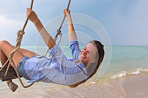 Summer solar portrait of fashion of a way of life of the young stylish woman,sitting on a swing on the beach,carrying lovely fashi