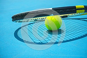 Summer sport concept with tennis ball and racket on blue hard tennis court.