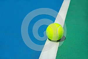 Summer sport concept with tennis ball on white line on hard tennis court.