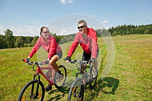 Summer - Sportive couple riding bike in meadow